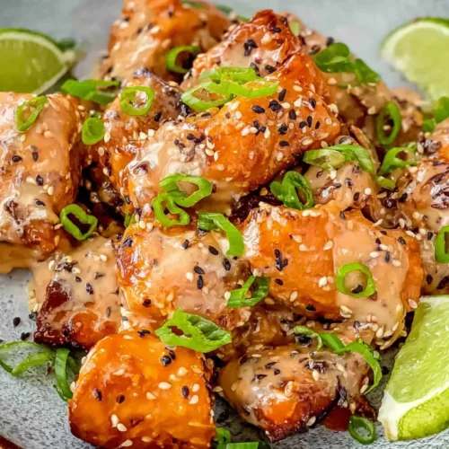 A plate of Bang Bang Salmon drizzled with a creamy, spicy sauce and garnished.