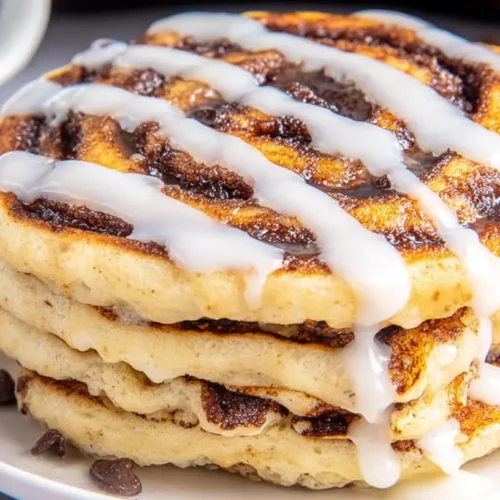 A stack of fluffy cinnamon roll pancakes topped with glaze
