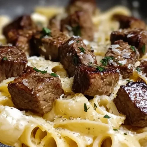 A close-up of a serving of steak and parmesan pasta garnished with fresh herbs.