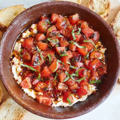 A vibrant bruschetta dip in a ceramic bowl, garnished with fresh herbs