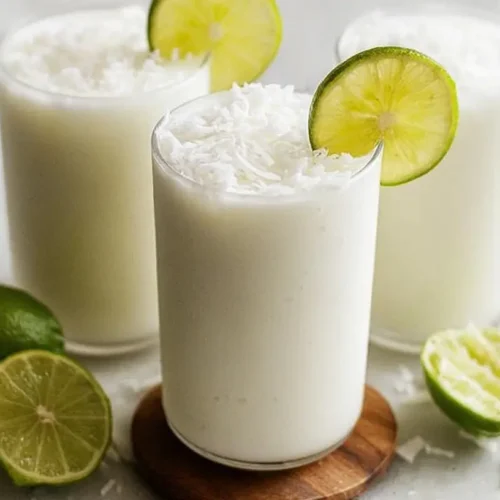 A refreshing glass of Colombian coconut limeade served with ice and a lime wedge.