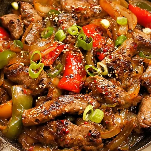 Close-up of sizzling Chinese pepper steak with tender beef and vibrant onions on a hot plate.