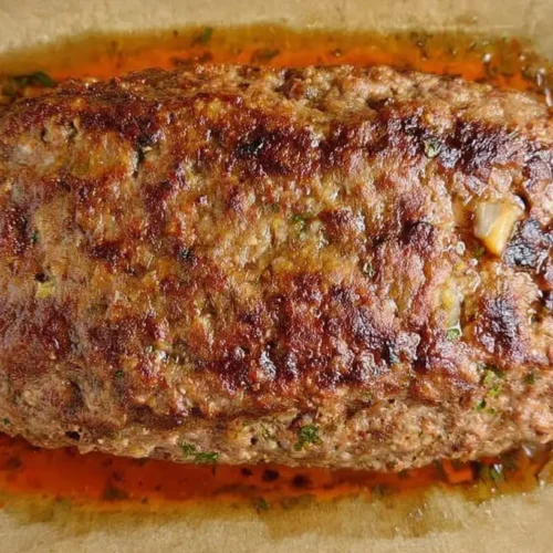 A serving of clean eating meatloaf on a white plate with steamed vegetables.